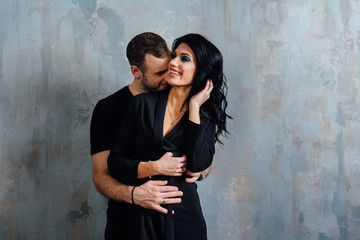 Young stylish beautiful gorgeous couple, against the gray wall loft in the studio or at home.