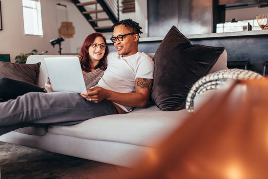 Couple relaxing on sofa at home with laptop