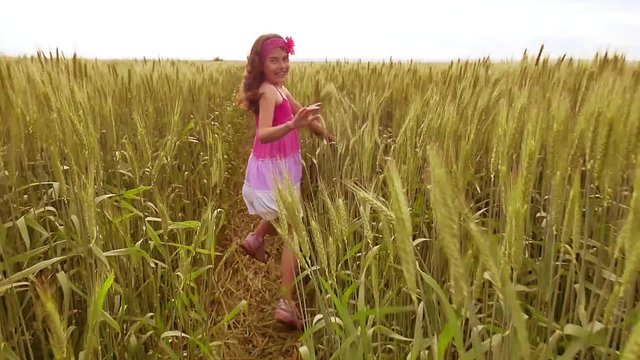 happy running kid girl on a wheat field in the sunlight. girl child running through the yellow field of outdoors wheat slow motion video