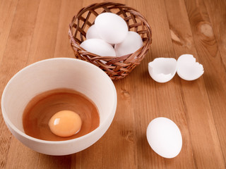 Basket with eggs, wooden bowl with yolk on a wooden table
