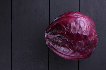 Purple cabbage on a dark wooden background, a whole cabbage on wooden planks of dark, purple vegetables, vegetarian food, copy space, a top view of vegetables in the style of minimalism