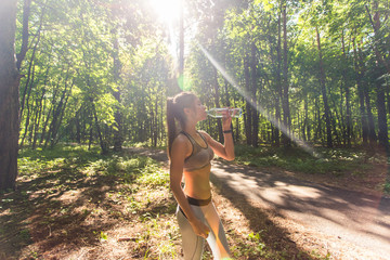 Fitness beautiful woman drinking water and sweating after exercising on summer hot day in park....