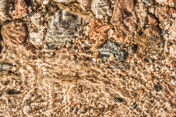 sand, stones of different size and leaves under the water in the sunlight, abstract background