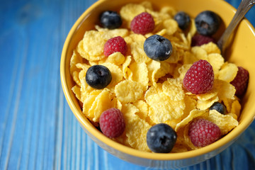 Cornflakes with berries raspberries and blueberries on blue wooden background.
