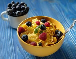 Cornflakes with berries raspberries and blueberries on blue wooden background.