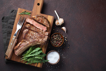 Grilled cowboy beef steak, herbs and spices on a dark stone background. Top view with copy space...
