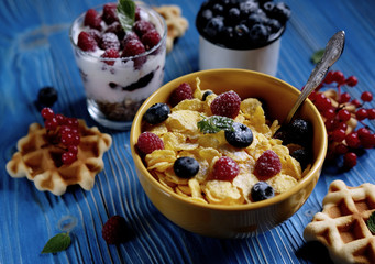 Healthy breakfast with corn flakes, berries, waffle and milk on blue background.