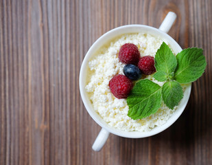 Cottage cheese with raspberries and blueberries in a bowl for healthy breakfast with ripe berries over rustic wooden background. Top view.