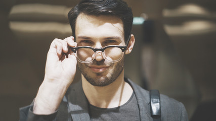 A closeup of a young smiling bearded man looking at the camera through his eyeglasses