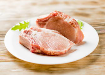Raw pork brisket, ribs on a white plate on a wooden background.