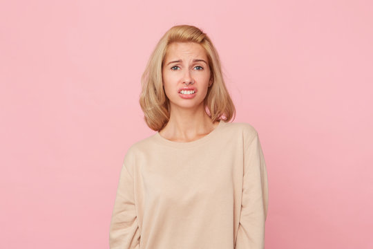 Dissatisfied female model frowns face, has disgusting expression,  expresses non compliance, irritated with somebody, wears yellow sweater. Negative emotion concept. Isolated over pink background