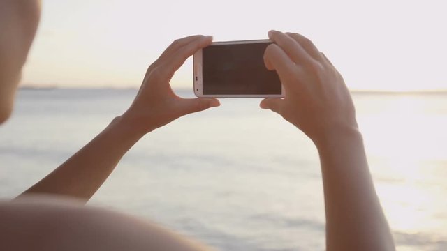 Tourist taking photograph of sunset on beach with mobile phone. View from woman using smartphone. Woman using smart phone girl outside.