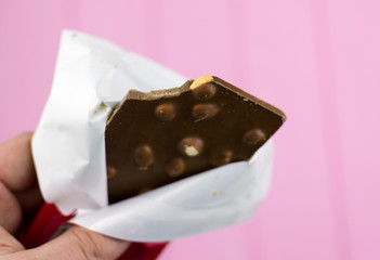 A bitten chocolate bar with nuts on a pink background.