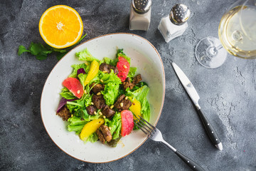 Tasty salad with citrus, lettuce and grilled chicken liver in a plate.