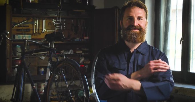Well-groomed handsome bearded master hipster, specialist in bicycles, repairing a bicycle in his workshop, wheels, frame, spokes, the background of tools. Concept: pro bike, cycle passion, lifestyle.
