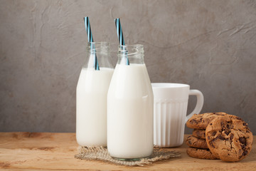 Two bottles of milk and chocolate chip cookies on dark background with copy space