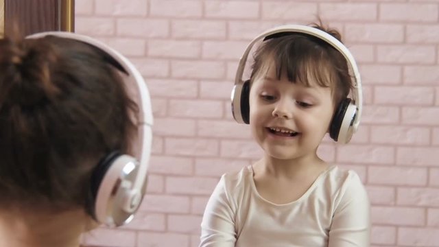A girl with headphones listens to music. A child in front of a mirror in headphones.
