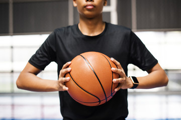 African American teenage boy holding a basketball on the court