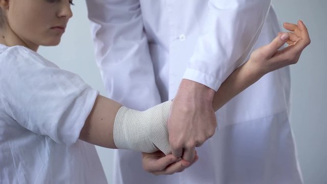 Doctor bandaging injured patient hand, first aid for sprain in trauma clinic