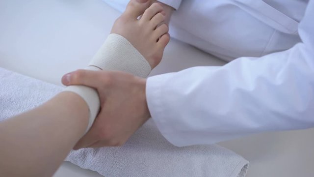 Doctor bandaging sprained ankle, running injury after workout, leg closeup