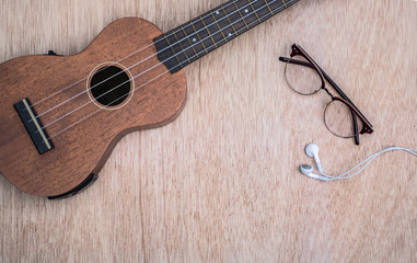 Fototapeta premium Ukulele with glasses and headphone on wood background.