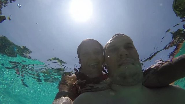Bottom view from the water of young couple taking a selfie in the Swimming Pool against the sun and water droplets. 1920x1080