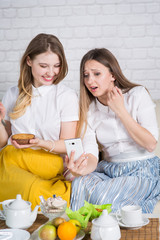 Obraz na płótnie Canvas Two young girls are sitting on the couch and making selfi,