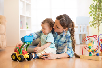 Little baby boy and mom playing on the floor with tractor toy