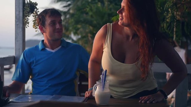 A young girl with a big chest sits at a table in a cafe and kisses her man. slow motion. 1920x1080. full hd