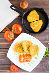 Crispy hash browns on a plate and in a pan and tomatoes on a wooden table. Top view