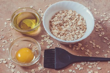 Bright egg yolk, oatflakes, olive oil, brush for mask application. Natural  ingredients for homemade beauty care on a beige background.  Preparation of home face masks.