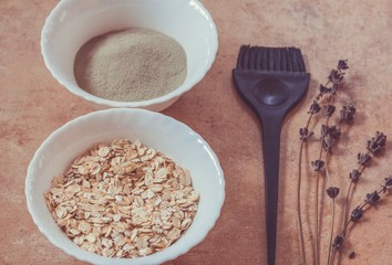 Oat flakes, green cosmetic clay,  brush for mask application. Natural  ingredients for homemade beauty care on a beige background.  Preparation of home face masks.