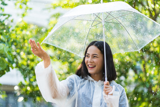 Rainy day asian woman wearing a raincoat outdoors. She is happy.She used her hand to touch the rain.