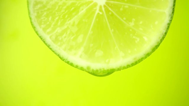 Close-up of a slice of lime, a drop of water falls. The fruit gives off freshness and juice filling. Concept of fresh fruit
