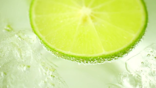 Close-up of a refreshing drink with bubbles interacting with ice and lime. Cold cocktail with lime.