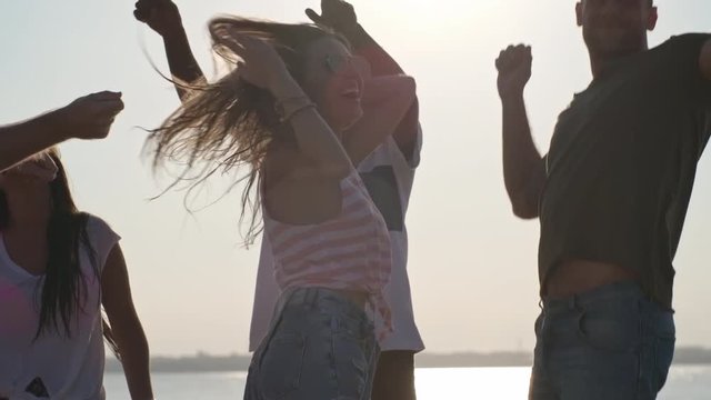 Tilt down of laughing group of friends  dancing and partying on beach on hot summer day
