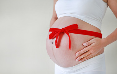 Close up belly of pregnant woman with red ribbon.