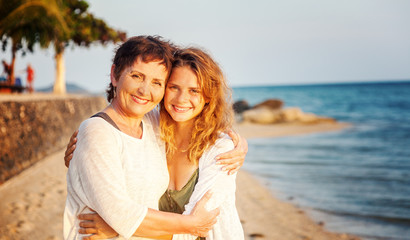 Obraz premium A beautiful mature woman with her adult daughter is walking along a tropical beach, relaxing together. Mothers Day