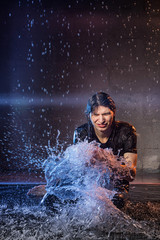 Attractive young man in black wet clothes under the rain and splash of water, studio photo