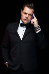 Portrait of confident handsome elegant stylish businessman with bow-tie showing on his brain on black background in studio