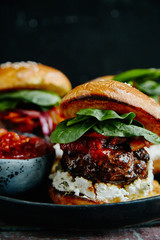 Burgers with grilled beef patties, cream cheese and spinach on classical bun. Dark rustic wooden background