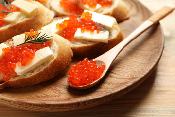 Delicious sandwiches and spoon with red caviar on wooden plate, closeup