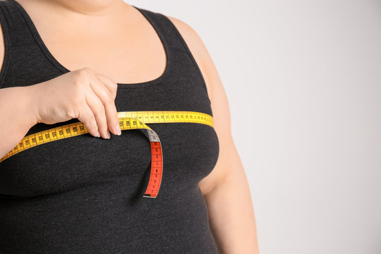 Overweight woman with measuring tape on light background