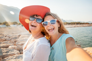 An attractive middle-aged woman with her adult daughter doing selfie on the beach, vacation and...