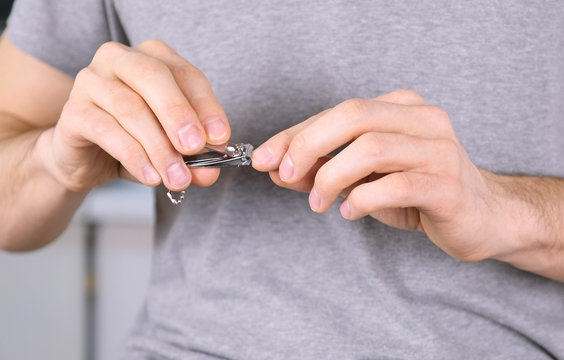 Man Is Cutting His Nails By Clippers. Close-up Hands.Grey T-shirt In The Background.