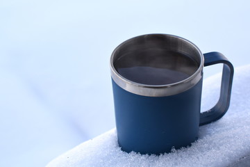 blue metall mug with hot drink in winter snow
