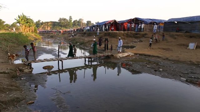 A crowd of people cross a small bridge over a ditch at the border of Bangladesh and Myanmar