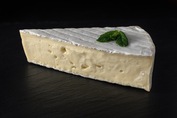 Fresh Brie cheese on black stone board with herbs.