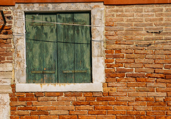 Window with green shutters on red brick wall of houses. Italy, Venice, Burano