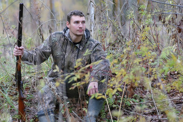 Man in camouflage and with guns in a forest belt on a spring hun